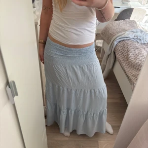 Ljusblå långkjol - Säljer en ljusblå långkjol med elastisk midja och volangdetaljer. Kjolen har en luftig och bekväm passform, perfekt för varma dagar. Den är tillverkad i ett lätt material som ger en fin rörelse.