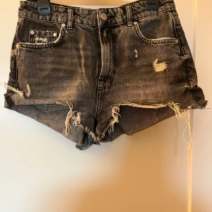Svarta jeansshorts från Zara - Snygga svarta jeansshorts från Zara med slitna detaljer och fransar. De har en klassisk femficksdesign och knappgylf. Perfekta för en avslappnad stil.