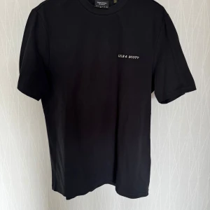 Svart t-shirt från Lyle & Scott - Snygg svart t-shirt från Lyle & Scott med liten logga på bröstet. Perfekt för en stilren look. Tillverkad i mjukt material för extra komfort. Tröjan är inte använd, så i nyskick. 