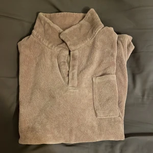 Beige kortärmad frotté skjorta - Säljer en beige kortärmad frotté skjortafrån. Tröjan har en mjuk och bekväm känsla med en liten bröstficka och en unik krage. Perfekt för en avslappnad stil. Hör av dig vid intresse!