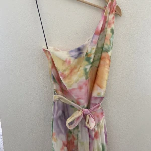 Söt klänning från H&M - Säljer en fin klänning från H&M med ett vackert mönster i flera färger. Klänningen har en oneshoulder-design och ett knytband i midjan för en smickrande passform. Perfekt för sommarens festligheter!