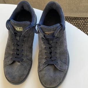 Blå sneakers från Polo - Snygga grå sneakers från Polo i mocka med klassisk snörning. Perfekta för en stilren look. De har en rund tå och en diskret logga på sidan.