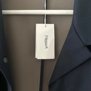 Mörkblå jacka från Filippa K - Säljer en stilren mörkblå jacka från Filippa K. Jackan har en klassisk design med långa ärmar och en elegant krage. Perfekt för en sofistikerad look.