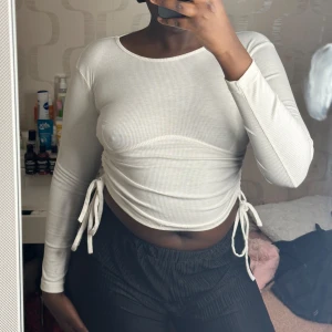 Vit ribbad långärmad topp - Säljer en stilren vit ribbad topp med långa ärmar och knytning i sidorna för en justerbar passform 🤍