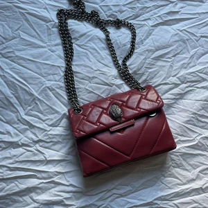Vinröd axelväska från Kurt Geiger - Snygg axelväska från Kurt Geiger med quiltat mönster och en elegant kedjerem. Överlag bra och skapligt använd, tecken på användning finns dock i i väskan hörn samt på ugglan men inget som syns på långt håll. Kvitto och påse tillkommer, bara att höra av sig vid frågor. Pris kan givetvis diskuteras!