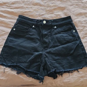 Svarta jeansshorts från H&M Divided - Snygga svarta jeansshorts från H&M Divided med fransiga kanter och klassisk femficksdesign. Perfekta för en avslappnad stil med en touch av edge. Passar utmärkt till sommarens alla äventyr.