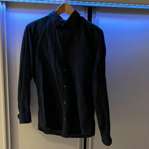 Mörkblå linneskjorta  - Snygg mörkblå långärmad skjorta med klassisk krage och knappar framtill. Perfekt för en stilren look. Passar bra till både jeans och kostymbyxor.