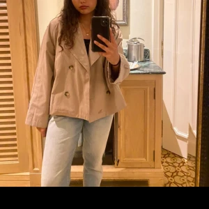 Beige trenchcoat Nelly  - Säljer en stilren beige trenchcoat med dubbelknäppning. Jackan har en lös passform och långa ärmar, perfekt för en chic look. Passar bra till både jeans och mer formella outfits.