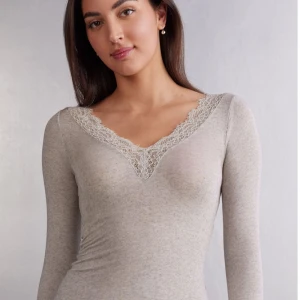 Ljusgrå långärmad topp med spets - Säljer en ljusgrå långärmad topp med v-ringning och fina spetsdetaljer längs halsringningen. Toppen är figurnära och passar perfekt till lager-på-lager eller som den är. Buds!