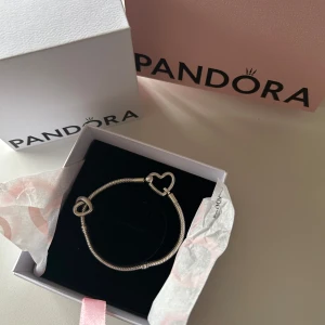 Silverarmband från Pandora med hjärtformad detalj - Elegant silverarmband från Pandora med en hjärtformad detalj. Perfekt som en stilren accessoar för att komplettera din look. Levereras i originalförpackning. KVITTO FINNS