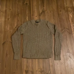 Brun stickad tröja från Bondelid - Säljer en snygg brun stickad tröja från Bondelid med klassiskt flätmönster. Tröjan har långa ärmar och en rund halsringning, perfekt för kyligare dagar. Ett tidlöst plagg som passar i garderoben året runt.