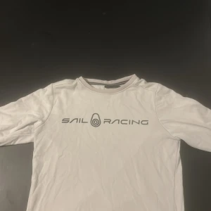 Vit långärmad tröja från Sail Racing - Säljer en vit långärmad tröja från Sail Racing med tryck på framsidan. Aningen urtvättad, knottrig på insidan med ser bra ut utifrån.