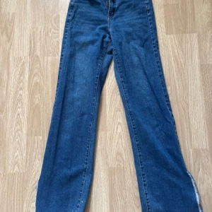Blå jeans med slits - Snygga blå jeans med hög midja och slits vid bensluten. De har en klassisk femficksdesign och en rak passform som ger en avslappnad look. Perfekta för en trendig stil.