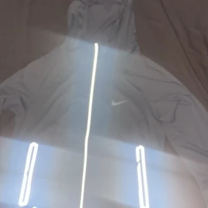 Grå nike miller jacka - Säljer en grå nike miller från Nike med huva och reflekterande detaljer. Jackan har dragkedja framtill och sidofickor med dragkedjor. Material är väldigt tunnt, den är 100% autentisk,helt ny med storlek S,perfekt för sommaren 