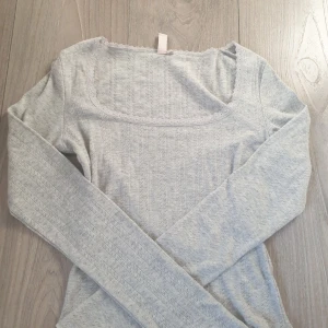 Ljusgrå långärmad topp från Nelly - Säljer en ljusgrå långärmad topp från Nelly med ett diskret mönster och spetsdetaljer runt halsringningen. Perfekt för en stilren look. 👚💗