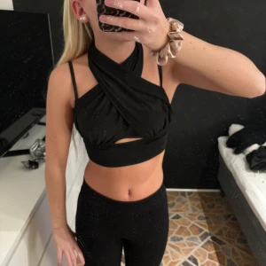 Svart omlott topp - Snygg svart omlott topp med halterneck-design och smala axelband. Toppen är croppad och har en unik omlott-detalj framtill. Perfekt för en kväll ute eller en festlig tillställning.