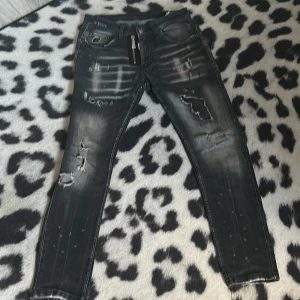 Svarta slitna jeans - Säljer ett par svarta jeans med slitningar och en cool, tvättad look. De har en dragkedja fram och är i en tight passform. Perfekta för en trendig stil!