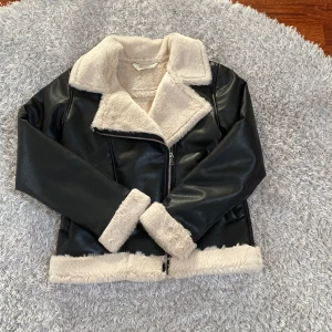 Svart skinnjacka med päls från H&M - Säljer en snygg svart skinnjacka från H&M med mjukt vitt päls. Jackan har en dragkedja framtill och är långärmad med päls vid ärmslut och krage. Perfekt nu när våren kommer! 