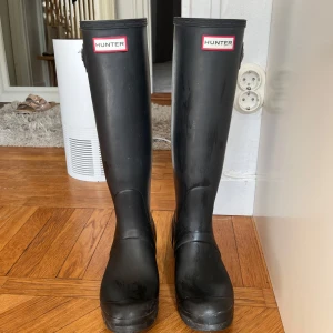 Svarta stövlar från Hunter - Säljer ett par klassiska svarta stövlar från Hunter. De är höga med en justerbar rem upptill och har en rund tå. Perfekta för regniga dagar och håller fötterna torra och bekväma.