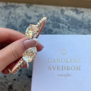Armband från Caroline Svedbom - Elegant armband från Caroline Svedbom med en tvinnad design i guldton. Armbandet pryds av två stora, gnistrande kristaller i varje ände som ger en lyxig känsla. Perfekt för att lyfta vilken outfit som helst.