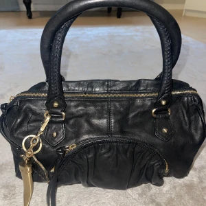 Svart skinn handväska från Botkier - Snygg svart handväska i skinn från Botkier med guldfärgade detaljer och dragkedja. Väskan har två handtag och en praktisk innerficka med dragkedja. Perfekt för att bära dina dagliga nödvändigheter med stil. Kom med bud! 