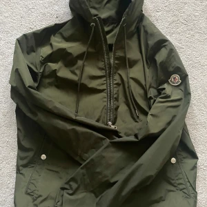 Moncler windbraker - Säljer en snygg grön vindjacka från Moncler med huva och dragkedja. Jackan har långa ärmar och en broderad Moncler-logga på ärmen. Perfekt för blåsiga dagar! Vid snabb affärer så kan ja gå ner i pris!