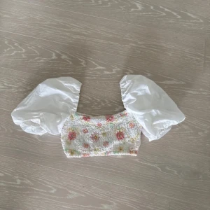 Blommig topp med puffärmar från Zara - Vlommig topp från Zara med stora vita puffärmar. Toppen har en croppad passform💕 Aldrig använd så är i nyskick! Jättefin nu till våren/sommaren! I storlek xs men passar S
