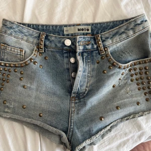 Jeansshorts med nitar  - Snygga jeansshorts med coola nitar längs fickorna och fransiga kanter. Perfekta för en avslappnad stil med en touch av edge. 
