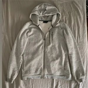 Grå sail racing hoodie  - Säljer en stilren grå hoodie med dragkedja och huva. Perfekt för en avslappnad look. Den har en liten logga på bröstet och är tillverkad i mjukt material för extra komfort. Den är i storlek 170 men passar även 160 