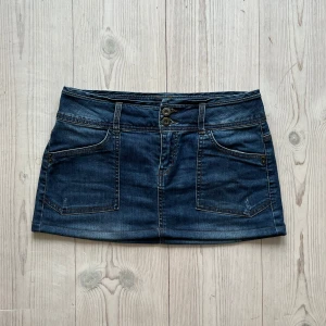 Mörkblå lågmidjad jeanskjol  - Blå lågmidjad jeanskjol från Camieu i fint skick. Kan inte hitta storlek men skulle säga S, kanske även kan passa M. Tvärs över midjan är det 38 cm och den är 28 cm lång. Använd gärna köp nu!