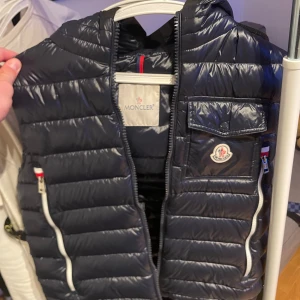 Mörkblå dunväst från Moncler - Snygg mörkblå dunväst från Moncler med dragkedja och praktiska fickor. Perfekt för kyligare dagar. Klassisk design med Moncler-logga. kan mötas upp runt stockholms områderna och är även öppen för byten skriv om det är frågor angående västen.
