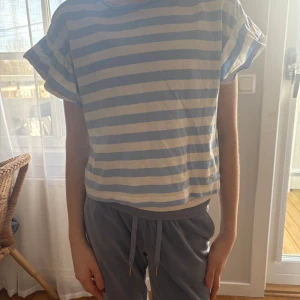 Randig t-shirt från Hampton Republic - Säljer en randig t-shirt från Hampton Republic i ljusblått och vitt. Den har korta ärmar med en lös passform och är perfekt för en avslappnad stil. Storleken är 146/152, vilket passar bra för ungdomar. Perfekt för vår och sommar!