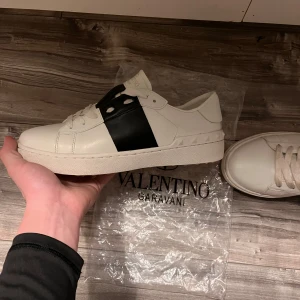 Valentino Garavani sneakers (HELT NYA) - Snygga vita Valentino Garavani sneakers med en bred svart rem över ovansidan. Skorna har en rund tå och är tillverkade i skinn. Perfekta för en stilren look. Skicket är 10/10 helt nya! Priset kan diskuteras vid snabb affär Hör gärna av er om frågar och prisförslag Mvh//Theo🙂