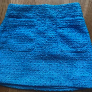 Blå kjol från H&M - Snygg blå kjol från H&M i ett texturerat material. Kjolen har en kort längd och en stilren design som passar perfekt för olika tillfällen. Den har en enkel passform och är lätt att matcha med olika toppar.