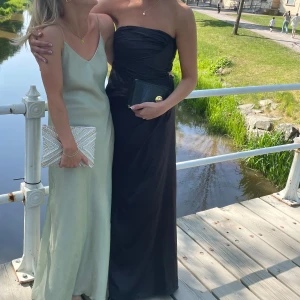 Svart axelbandslös balklänning -  svart axelbandslös långklänning med draperad detalj framtill.