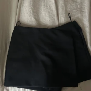 Svart skort  med minimalistisk design - Säljer svarta skorts med stilren och enkel look. Skortsen har raka linjer och två dekorativa fickor bak. Perfekt för dig som gillar en clean och klassisk stil. Passar till många olika outfits.