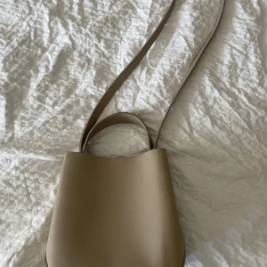 Beige axelväska från Gina Tricot - Säljer en stilren beige axelväska från Gina Tricot. Väskan har en enkel och modern design med både axelrem och handtag, perfekt för att bära över axeln eller i handen. 