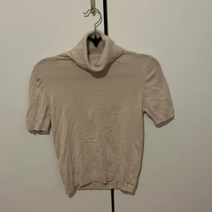 Beige polotröja med kort ärm från MNG - Säljer en beige polotröja från MNG i storlek S. Tröjan har korta ärmar och är tillverkad i ett mjukt, ribbat material som sitter bekvämt. Perfekt att styla med jeans eller kjol för en clean look.