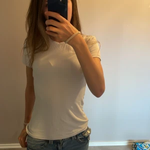 Vit basic t-shirt - En klassisk vit t-shirt med rund hals och korta ärmar. Modellen är figurnära och passar perfekt till jeans eller shorts. Tillverkad i mjuk bomull som känns skön mot huden. Köptes 3 månader sedan.