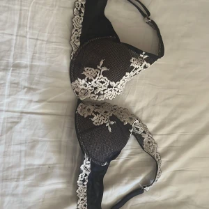 Svart spets-bh från Intimissimi - Säljer en svart bh från Intimissimi med vacker beige spetsdetalj och blommigt broderi. Bh:n har vadderade kupor och justerbara axelband. Perfekt för dig som vill ha något både snyggt och bekvämt.