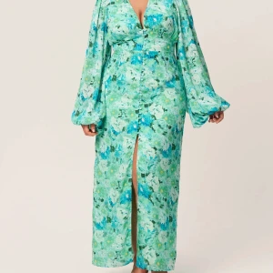 Grön blommig långklänning med slits - Säljer en härlig långklänning i gröna och blå toner med blommigt mönster. Klänningen av modellen ADOORE POSITANO DRESS i färgen MINT GREEN har långa puffärmar, v-ringning och en slits framtill. Den har markerad midja och knappar längs framsidan. Använd en kväll och jag kände mig jättefin. Obs liten i storleken. Om önskas medföljer ADOORE original förpackning i vacker större kasse eller kan slås in som present. 