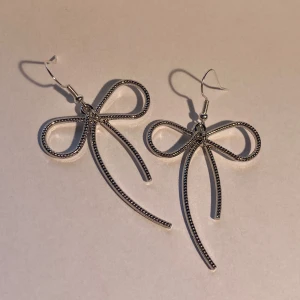 Silvriga örhängen i rosettform - Säljer ett par silvriga örhängen formade som stora rosetter. De har en tunn, elegant design och hängs i örat med krok. Perfekta för dig som vill ha örhängen med söt och trendig känsla. Funkar till alla tillfällen!