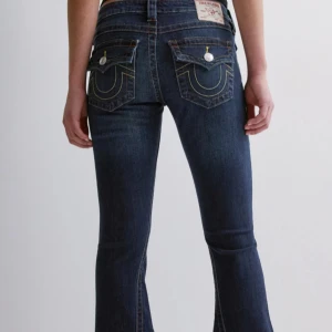 Joey low rise flare från True Religion - Säljer ett par mörkblå jeans från True Religion med bootcut passform (modellen Joey Low Rise Flare). Byxorna har låg midja, klassiska fickor med dekorativa sömmar och knappar bak. Storlek W26, passar XS-S och är stretchiga! Fint skick ❣️