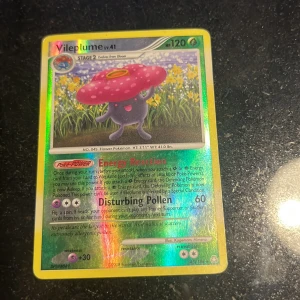 Vileplume - Detta är ett samlarkort från Pokémon-serien med Vileplume, en färgglad och glittrig holografisk design. Perfekt för dig som gillar Pokémon och vill utöka din samling med en klassisk karaktär från spelet och serien.
