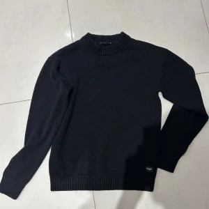 Svart stickad tröja från Jack & Jones - Säljer en svart stickad tröja från Jack & Jones i storlek XS. Tröjan har rund halsringning och långa ärmar med ribbade muddar vid ärmslut och nederkant. Perfekt för kyligare dagar och enkel att matcha med det mesta.