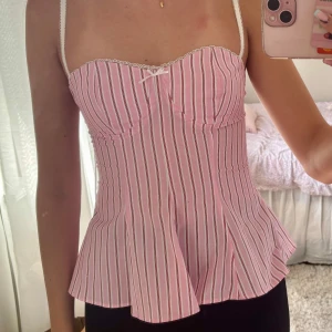 Rosa och vit randig korsettopp från Bershka - Supersöt korsettopp från Zara i rosa och vitt. Toppen har en liten rosett framtill och utsvängd nederdel. Endast testad, säljer då jag inte orkar returnera den🥲