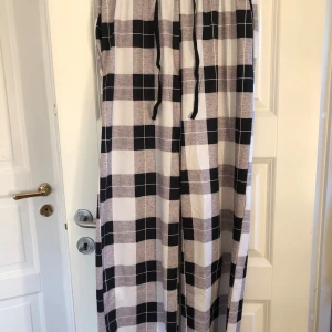 Svart, vit och grå pyjamasbyxa  - Säljer ett par vida pyjamasbyxor med svart, vit och grå rutigt mönster i storlek s/m. Byxorna har resår och snörning i midjan för extra komfort 🖤🩶🤍