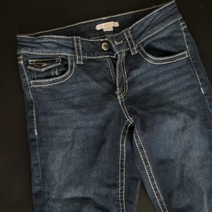 Mörkblå jeans  från Gina Tricot - Har aldrig använt. Mörkblå jeansbyxor från Gina Tricot med vita kontrastsömmar. Byxorna har normal passform och bootcut  ben. Perfekta för dig som gillar en enkel och tidlös jeansstil.