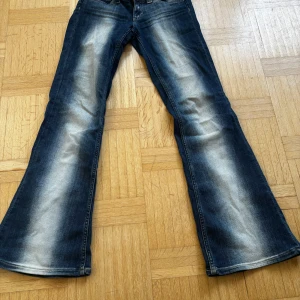 Blå bootcut jeans med slitningar (kvarg jeans) - Säljer ett par blå bootcut jeans med tydliga slitningar framtill och baktill. Jeansen är G RISE=Extremt lågmidjade Storlek 26 midjad och 30 längd