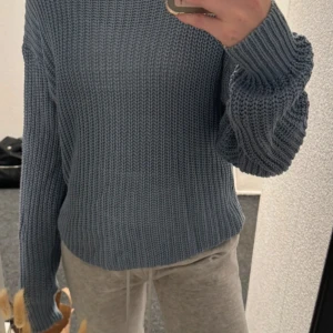 Blå stickad tröja från 157 - Mysig blå stickad tröja från 157 med grovstickad struktur. Tröjan har lång ärm och rund halsringning, perfekt för lager-på-lager. Enkel och stilren design som passar till många olika outfits.